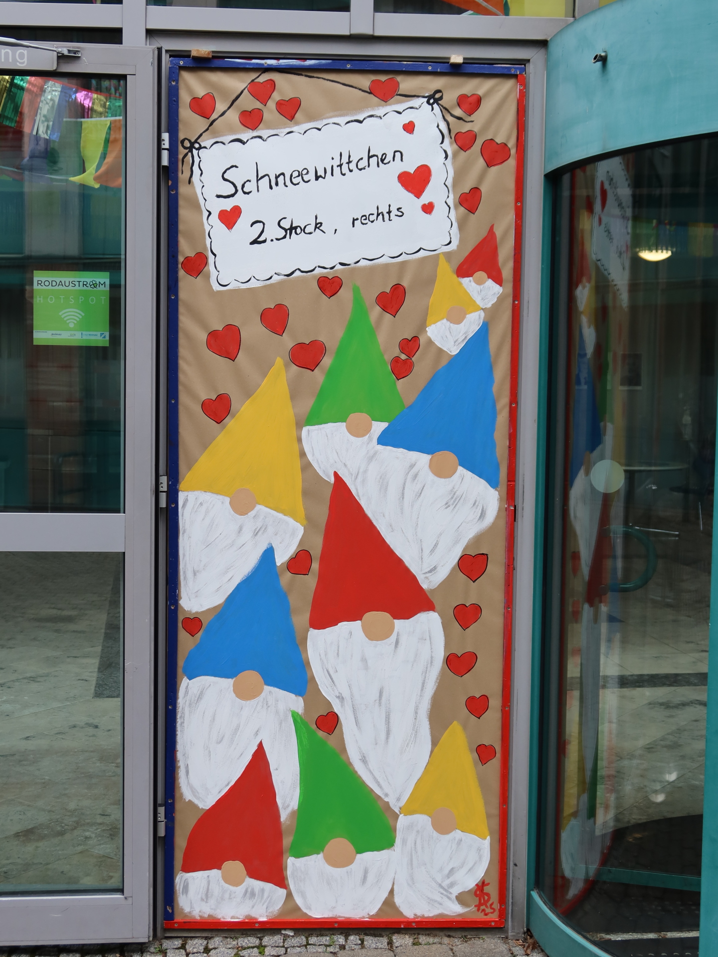 Décoration colorée de la porte de la mairie avec plusieurs nains en rouge, jaune et bleu sur un fond marron. En haut, on peut lire 'Blanche-Neige 2ème étage, droite'.