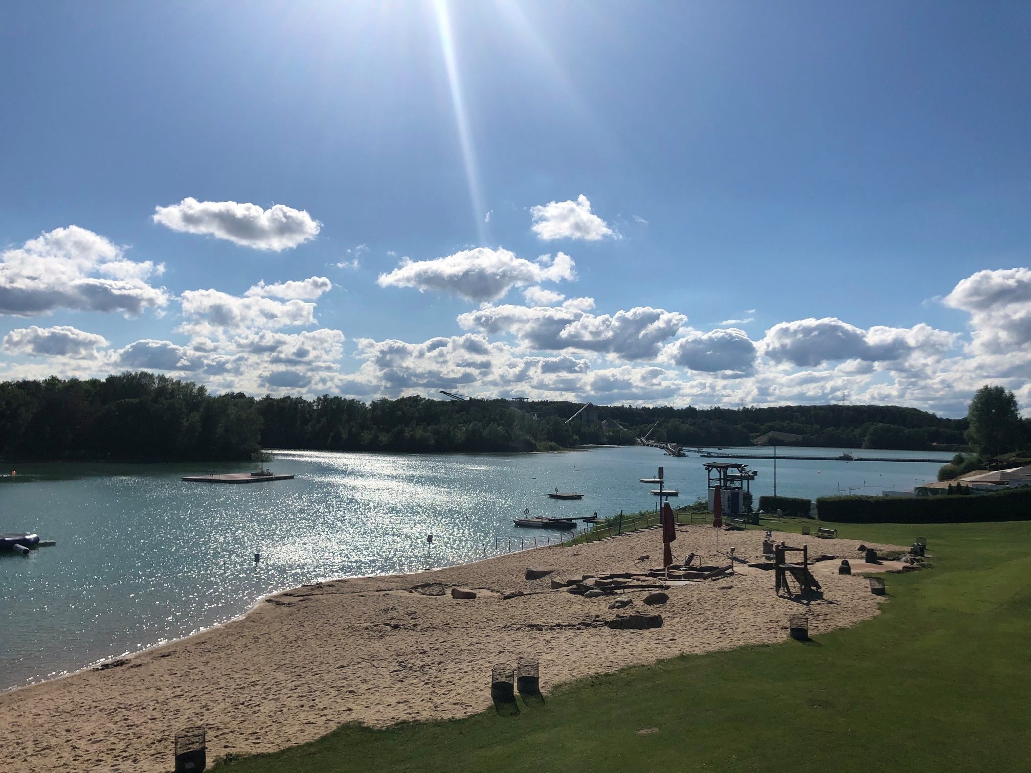 Plage de Rodgau Une plage avec des bateaux et un lac en arrière-plan, entourée de vagues douces et d'un rivage vert.