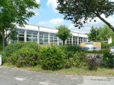 Vue du gymnase de l'école Freiherr-vom-Stein, entouré d'arbres denses et d'arbustes colorés.