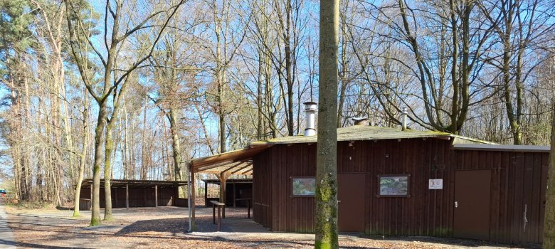 Centre de loisirs forestiers de Hainhausen A droite, on peut voir le bâtiment de gestion du centre de loisirs forestier de Hainhausen, avec en arrière-plan l'aire de repos couverte et l'esplanade ainsi que des arbres de la forêt.