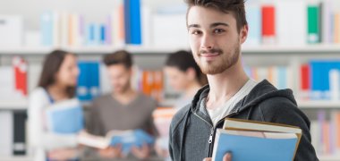 Un jeune étudiant en gestion publique dans une bibliothèque tient des livres dans ses bras et sourit Un jeune étudiant en gestion publique dans une bibliothèque tient des livres dans ses bras et sourit
