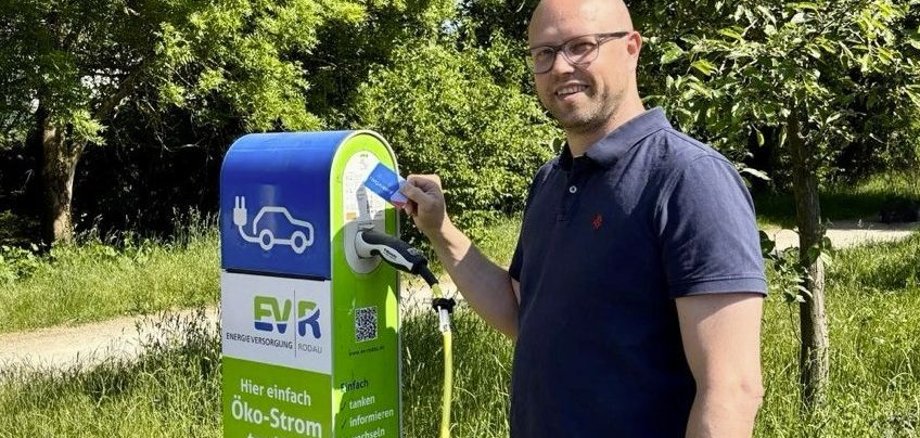 Recharger une voiture électrique avec la Rodgaucard Un homme portant des lunettes et un polo bleu recharge sa voiture électrique à une borne de recharge verte installée à l'extérieur