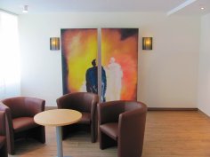 Salle d'adieu avec salon Au premier plan, trois sièges individuels en cuir. En arrière-plan, une image de deux personnes abstraites en noir et blanc.