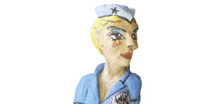 Scultura di un pilota seduto in uniforme blu, su un aereo. Materiale: quercia rossa, altezza circa 60 cm, anno: 2019, iscrizione: "Pop-A-Roc".