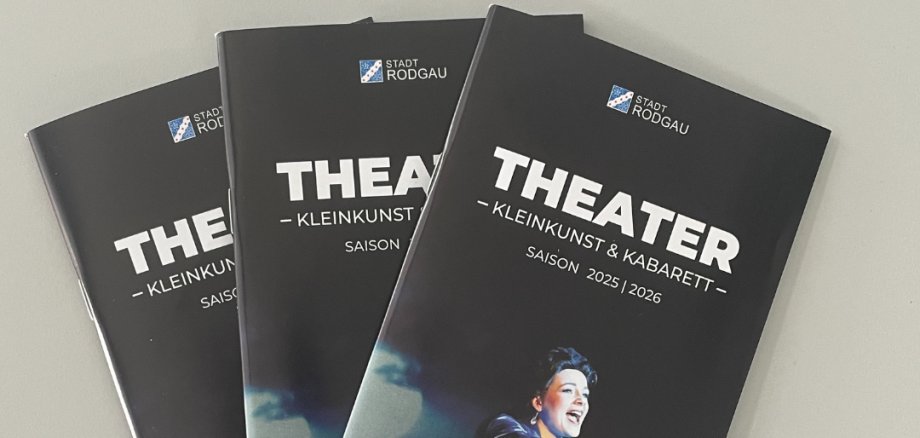 Tre opuscoli teatrali neri con il titolo "THEATER - KLEINKUNST & KABARET" per la stagione 2025/2026, con una persona in costume bianco.