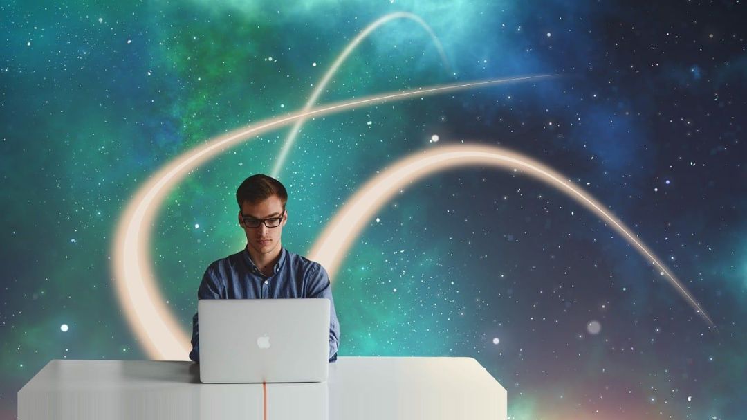 Un uomo con gli occhiali è seduto davanti a un computer portatile su uno sfondo con stelle e linee luminose