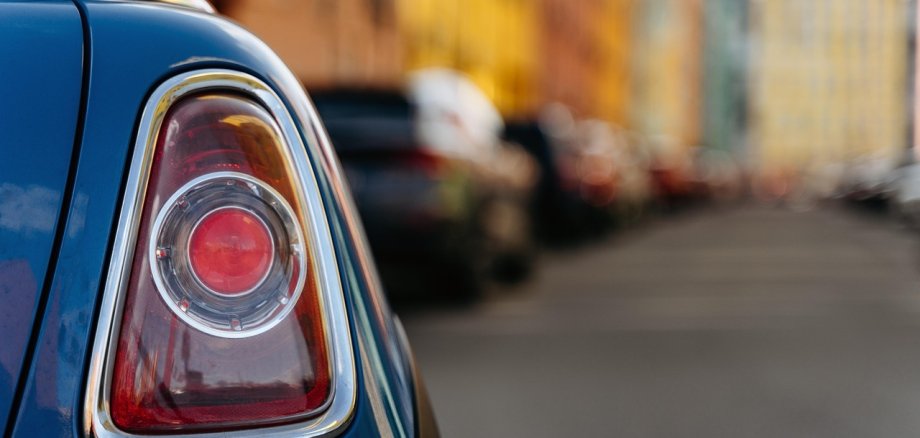 In primo piano si vede il fanalino di coda di un'auto, sullo sfondo un canyon stradale con case davanti alle quali sono parcheggiate molte auto.