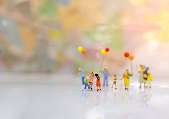 Gruppo di minuscoli personaggi con palloncini colorati su uno sfondo chiaro, davanti a uno sfondo sfocato e colorato