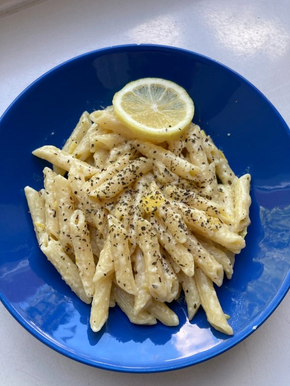 Piatto di penne in salsa cremosa, guarnite con pepe nero e una fetta di limone su un piatto blu.