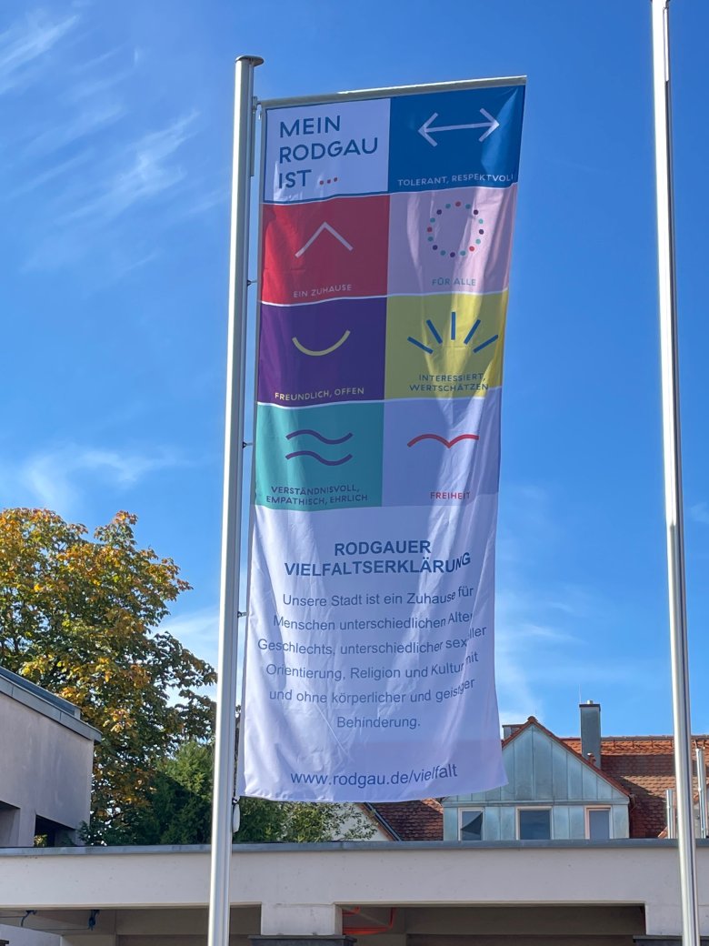 Bandiera della diversità con dichiarazioni sulla diversità a Rodgau, tra cui "La mia Rodgau è...", vari simboli e la Dichiarazione della diversità di Rodgau in Bürgermeister-Hermann-Sahrm-Platz