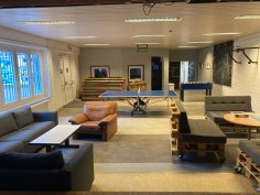 L'immagine mostra la grande sala del centro giovanile nel seminterrato con tavolo da ping pong, biliardino e posti a sedere.