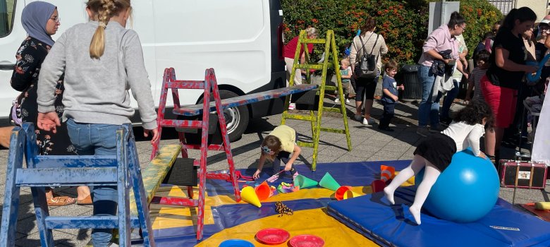 I bambini giocano in un parco giochi colorato I bambini giocano in un parco giochi colorato con scale, tappetini e una grande palla da ginnastica blu durante una festa all'aperto