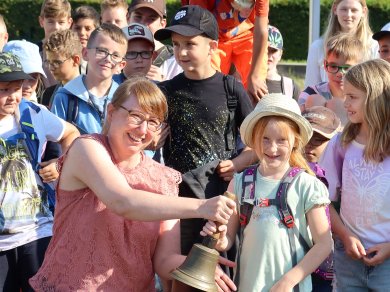 La signora Martin suona il campanello per aprire i giochi delle vacanze, circondata da bambini con zaini all'esterno
