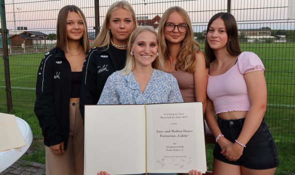 Cinque giovani donne si trovano all'esterno, davanti a una recinzione, una delle quali tiene in mano il libro d'oro con il premio per la danza jazz e moderna della formazione Calida.