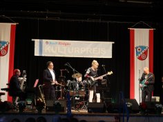 Banda musicale suona sul palco alla cerimonia di premiazione culturale della città di Rodgau con striscione e due bandiere rosse con stemma