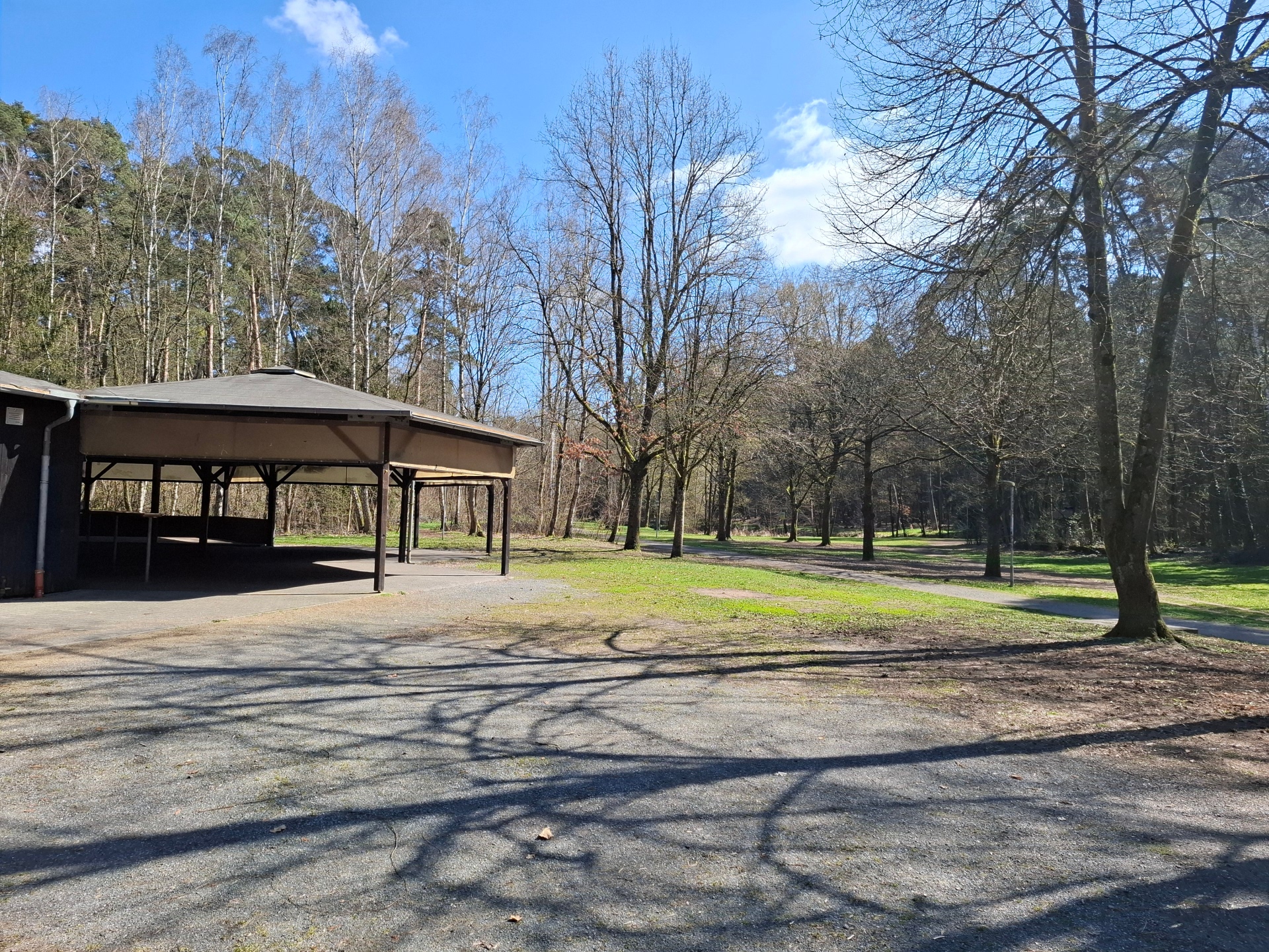 A sinistra dell'immagine si trova l'edificio coperto in legno del centro ricreativo della foresta, al centro e a destra il prato e la foresta con vista sul Gänsbrüh a Dudenhofen.