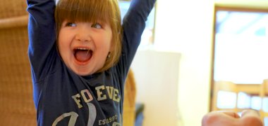 Bambino che ride alza le mani in aria - sullo sfondo un asilo nido