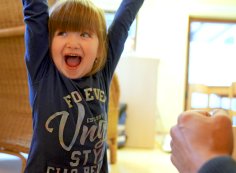 Bambino che ride alza le mani in aria - sullo sfondo un asilo nido