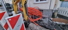 Un escavatore si trova davanti a una casa dove è stato scavato il marciapiede e posato un cavo in fibra ottica.
