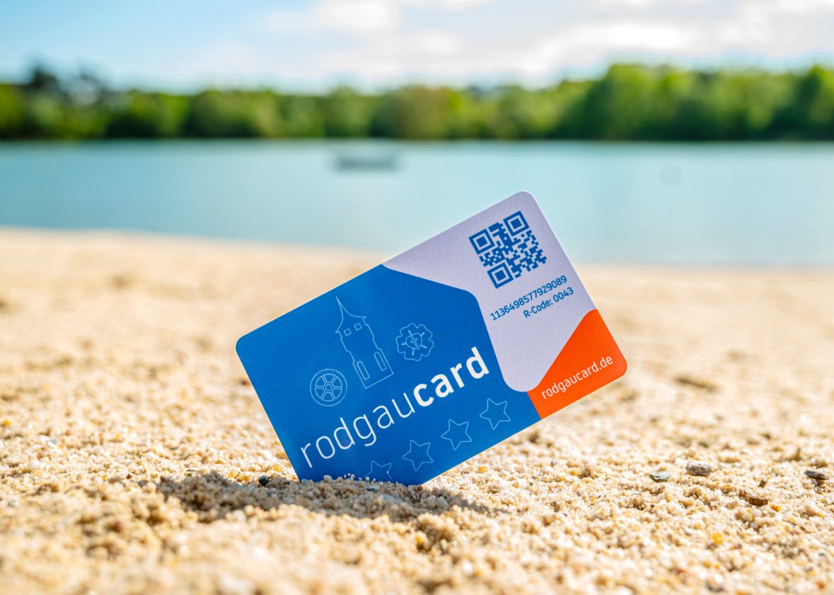 rodgaucard sulla spiaggia Cartoncino Rodgaucard conficcato in diagonale nella sabbia del lido con acqua sfocata e vegetazione verde sullo sfondo