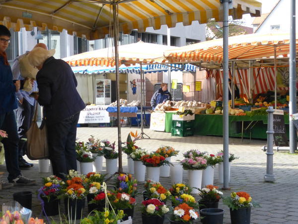 Mercato settimanale a Jügesheim con bancarelle di fiori, verdure e prodotti da forno sotto tende a righe