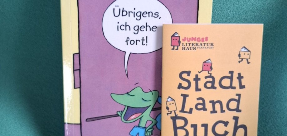 Książka dla dzieci "Przy okazji, odchodzę" i "Stadt Land Buch Książka dla dzieci z fioletową okładką i dymkiem z tekstem "A propos, wyjeżdżam" obok broszury z programem festiwalu książki dla dzieci i młodzieży "Stadt Land Buch".