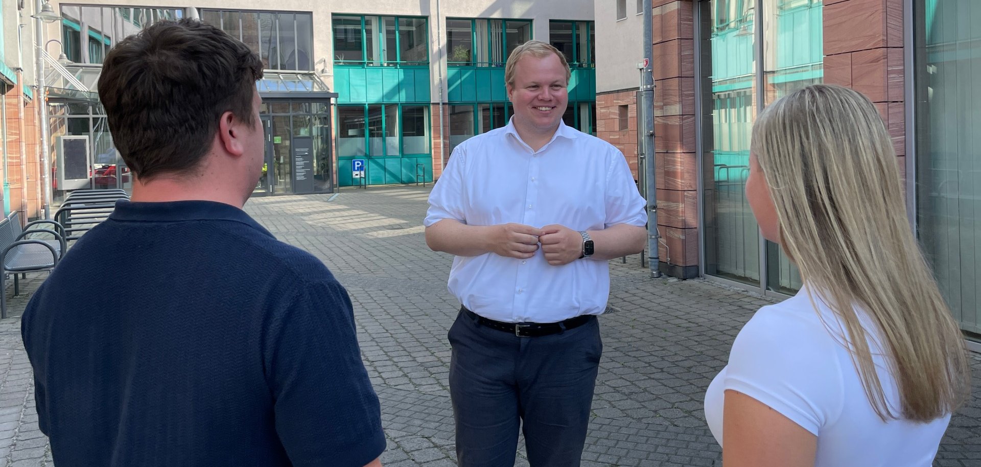 Burmistrz Max Breitenbach rozmawia z dwiema osobami na wewnętrznym dziedzińcu ratusza.