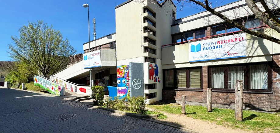 Widok z zewnątrz biblioteki publicznej Rodgau w Niederroden z rampą wejściową i kolorowymi muralami na betonowej ścianie.