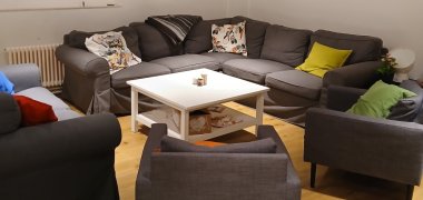 Centrum młodzieżowe W tym pokoju znajduje się szara narożna sofa i trzy fotele. Znajduje się na nich wiele kolorowych poduszek i biały stolik.