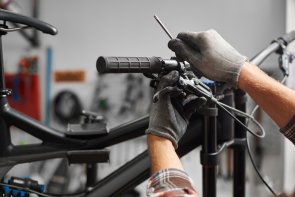 Naprawa roweru Mężczyzna w rękawiczkach reguluje za pomocą narzędzia hamulce na kierownicy roweru.