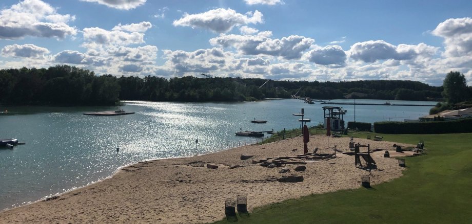 Plaża z łodziami i jeziorem w tle, otoczona łagodnymi falami i zielonym brzegiem.