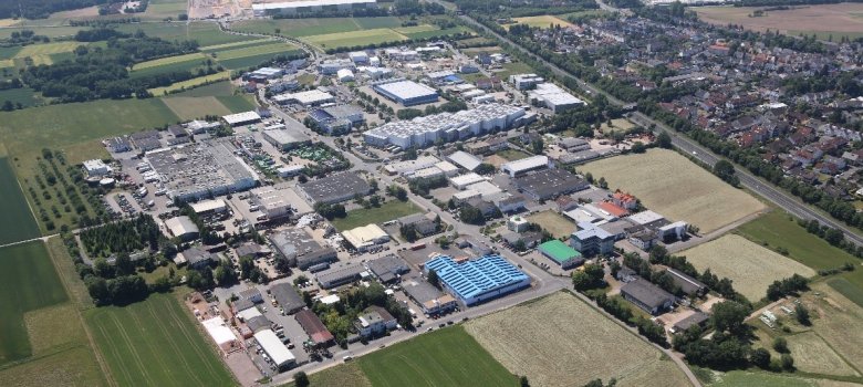 Widok z lotu ptaka na osiedle przemysłowe Jügesheim z różnymi budynkami przemysłowymi i magazynami, otoczone polami i sąsiednim obszarem mieszkalnym w tle.
