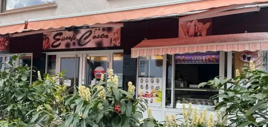 Gelataria com a inscrição "Eiscafe Costa" por detrás de plantas verdes em vasos