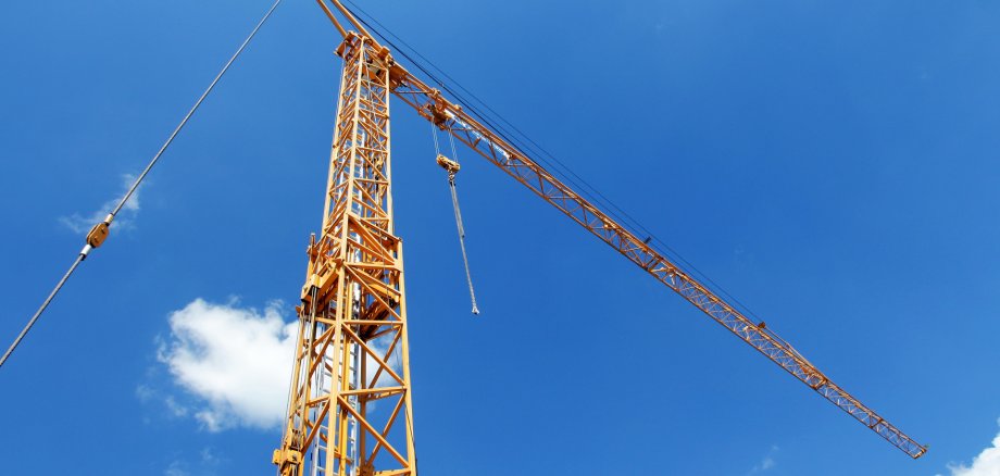 Grua de construção amarela alta em frente a um céu azul com algumas nuvens brancas