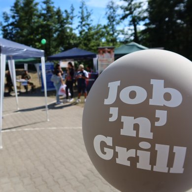 Feira de educação Balão com a etiqueta "Job 'n' Grill" em frente aos stands e visitantes de uma feira de educação ao ar livre