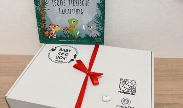 Caixa de informação para bebé branca com fita vermelha e livro "Leon's animal cold" com ilustrações de animais em fundo