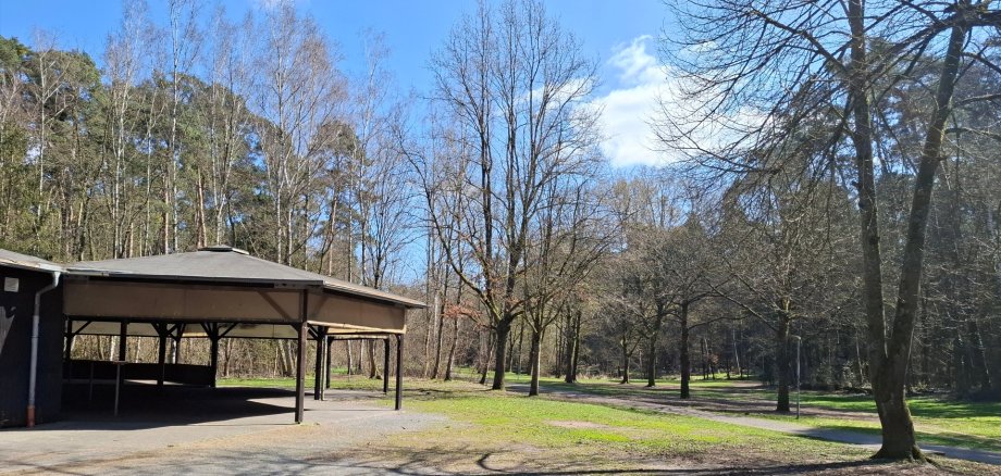 À esquerda da imagem está o edifício de madeira coberto do centro de lazer da floresta, no centro e à direita estão o prado e a floresta com vista para o Gänsbrüh em Dudenhofen