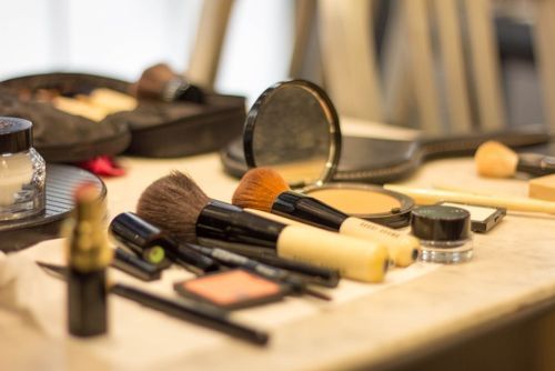 Pensule de machiaj, ruj, pudră compactă și alte produse cosmetice așezate pe o masă