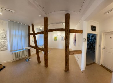 Galeria Rodgau Interiorul Galeriei Rodgau, cu pereți albi, mai multe opere de artă pe pereți și o structură din lemn cu două bârne în centru