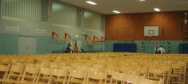 Gimnaziu Vedere interioară a sălii de gimnastică Carl-Orff-Schule cu multe scaune din lemn în rânduri ordonate.