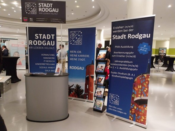 Stand de târg pentru educatori Stand de expoziție albastru al orașului Rodgau cu publicitate pentru cariere în educație. Lângă acesta sunt expuse broșuri. Alți expozanți ai târgului pot fi văzuți în fundal.