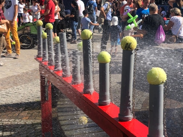 Çocuk partisi Zincirleri üzerinde tenis topları olan birkaç gri boru bulunan kırmızı bir su istasyonu. Arka planda bir partide çok sayıda insan var.