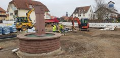 Im Vordergrund ist der Brunnen am Bürgerhaus in Dudenhofen, dahinter ein Bagger und daneben Bauarbeiter