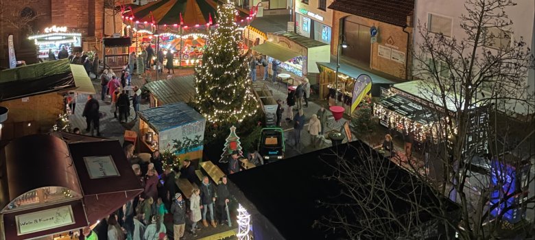 Rodgau'daki belediye binası meydanında ışıklandırılmış Noel ağacı, atlıkarınca ve tarihi binaların önünde pazar tezgahlarının yer aldığı akşam Advent pazarı.