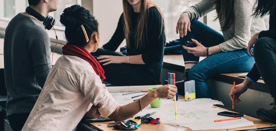 Мовне кафе Кілька молодих людей сидять за столом у мовному кафе, обговорюючи та працюючи разом на великому аркуші паперу з ручками та маркерами