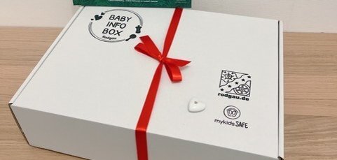 Біла інформаційна коробка для дитини з червоною стрічкою та книжкою Біла інформаційна коробка для немовлят з червоною стрічкою та книгою "Застуда тварин Леона" з ілюстраціями тварин на задньому плані