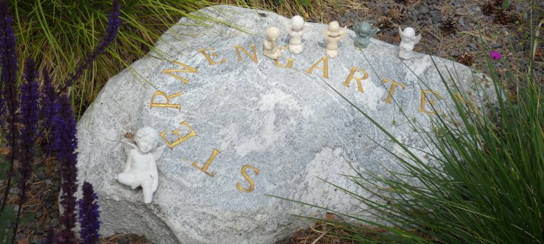 Ein Stein mit der Aufschrift Sternenkinder. Am oberen Rand sind kleine Engelsskulpturen zu sehen.
