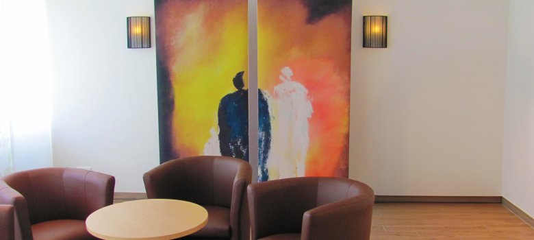 Verabschiedungsraum mit Sitzgruppe Im Vordergrund sind drei Ledereinzelsitze im Hintergrund ein Bild mit zwei abstrahierten Personen in schwarz und weiß.